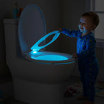 Abattant WC réducteur enfant ouvert par un enfant dans une salle de bain sans lumière mais illuminée par une LED de l'abattant
